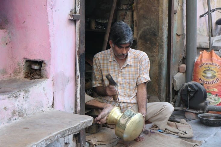 un ouvrier qui martèle des pots en métal à longueur de journée