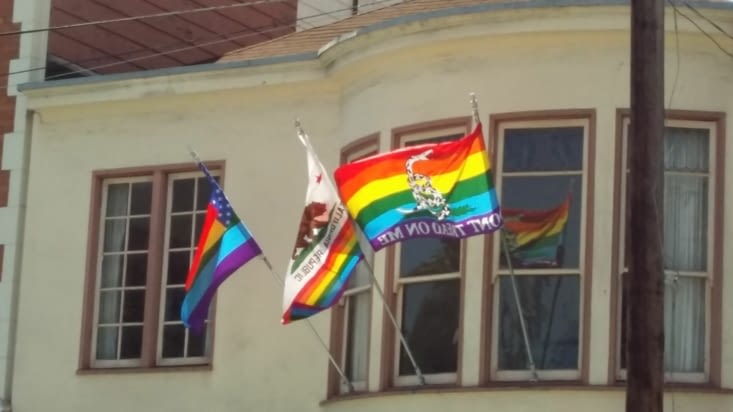 L étendard  du rainbow flag au côté ďu drapeau californien modifié et celui des usa modifi